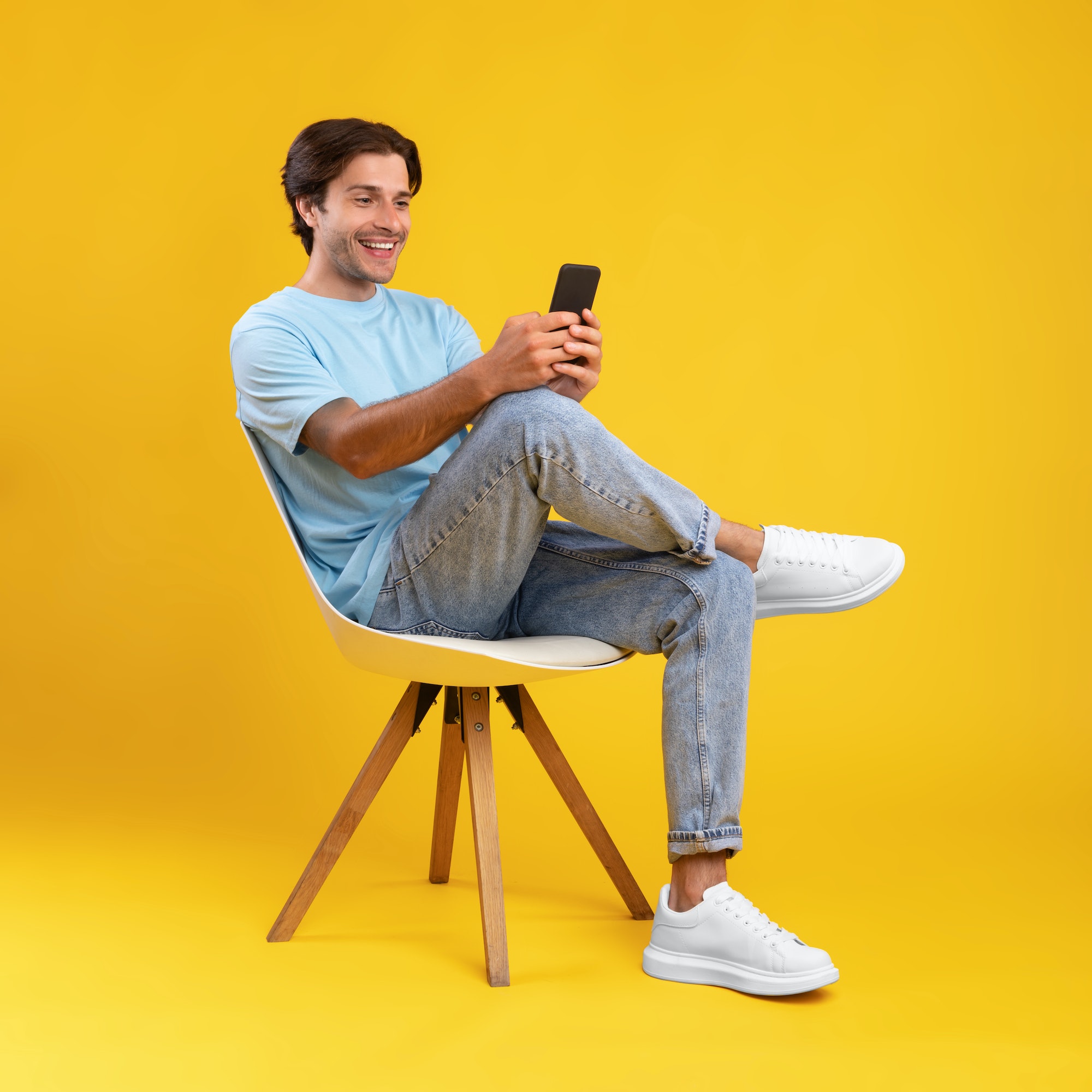 Happy guy using mobile phone at studio, sitting on chair