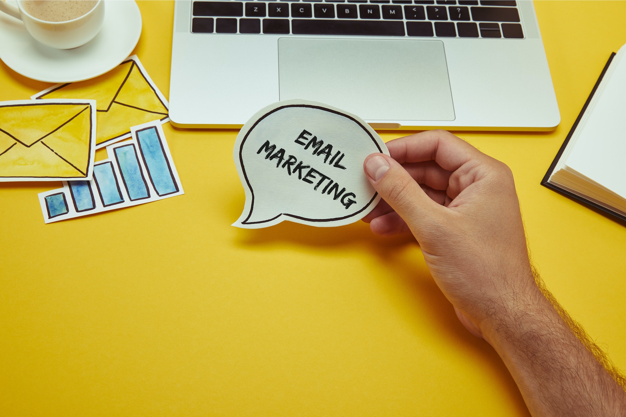 cropped image of man holding speech bubble with"email marketing" lettering near laptop